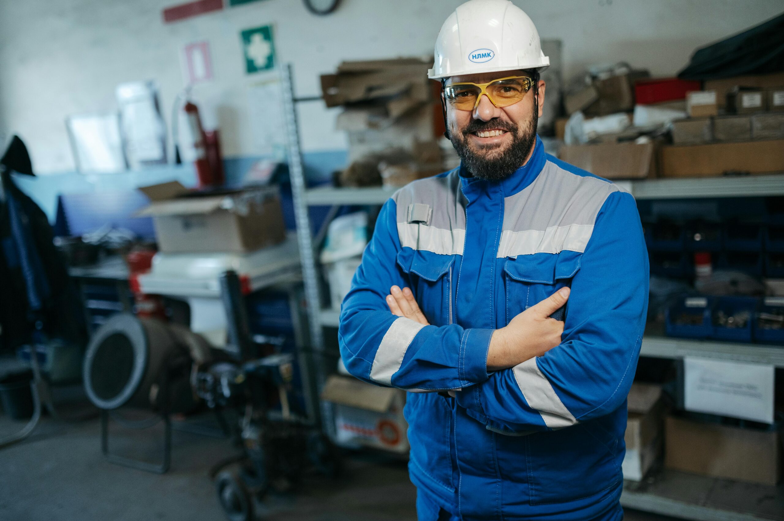 Smiling worker in blue uniform and hard hat standing in a factory setting in Russia.